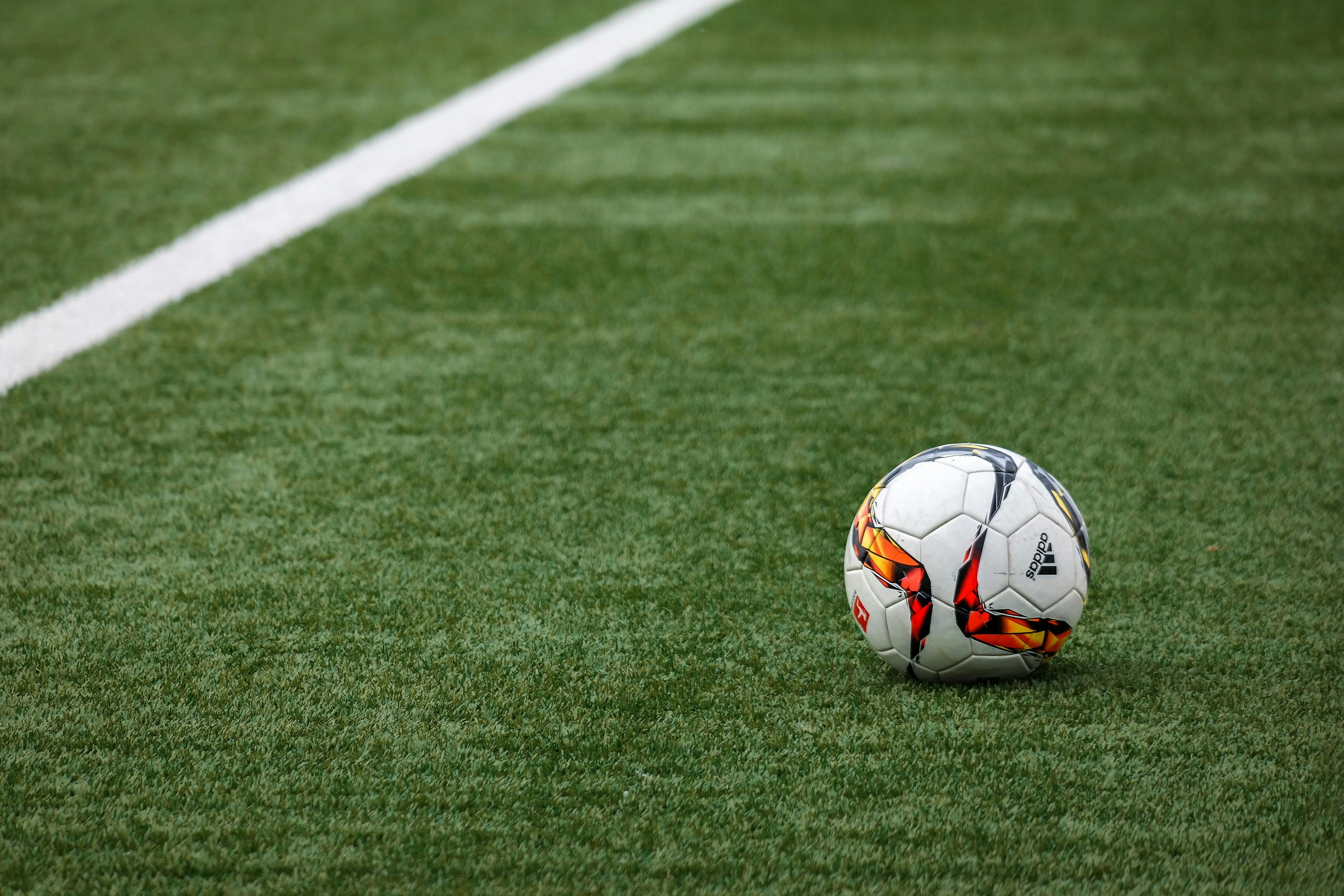 A soccer ball on a grass field with a white line in the background